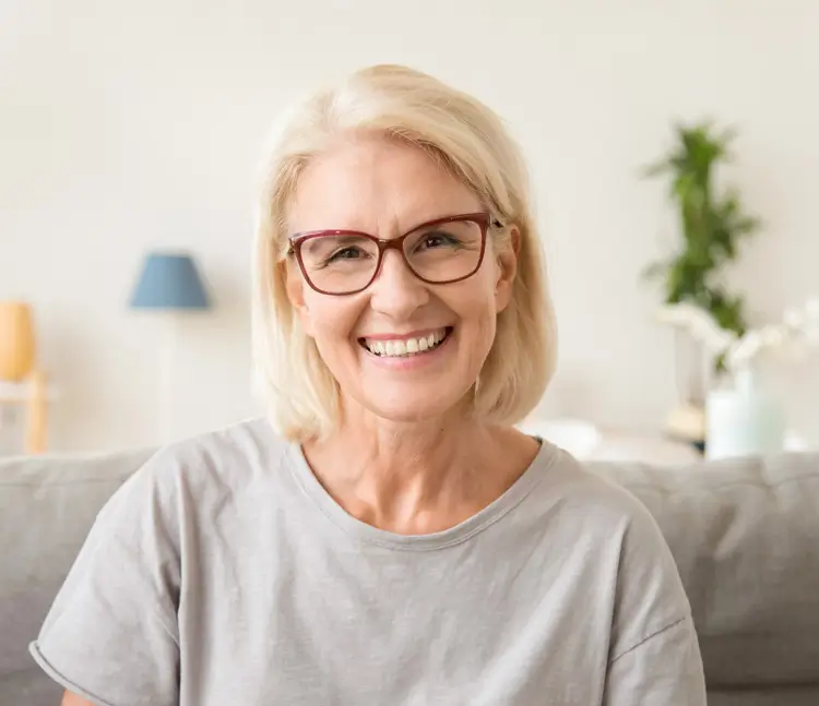 Portr&auml;t einer l&auml;chelnden Frau mit Brille in einem grauen T-Shirt auf einer Couch