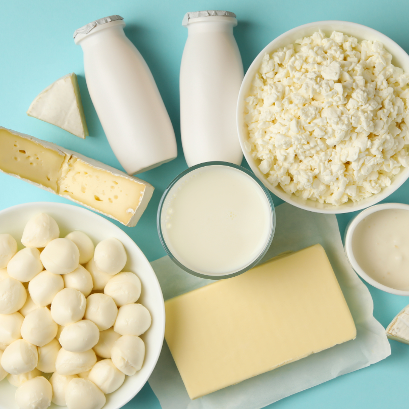 Verschiedene Milchprodukte auf blauem Untergrund, darunter Frischk&auml;se, Mozzarella-Kugeln, Butter, Milch in Glas und Flaschen, sowie K&auml;sest&uuml;cke