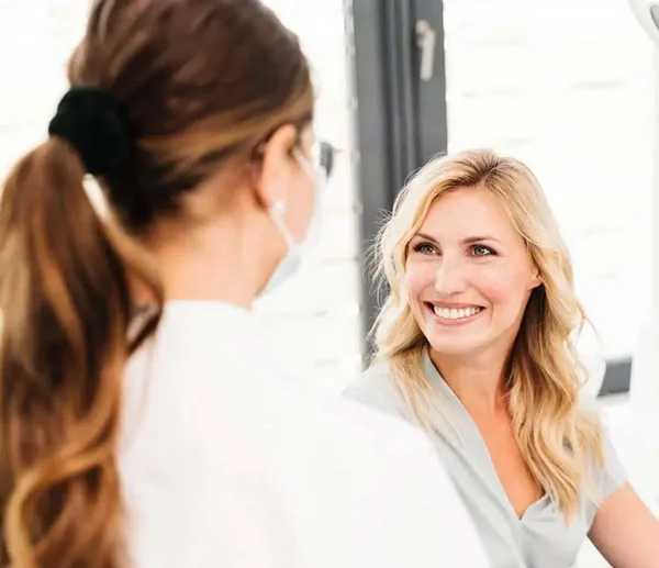Blick über die Schulter einer Zahnärztin auf eine lächelnde Patientin